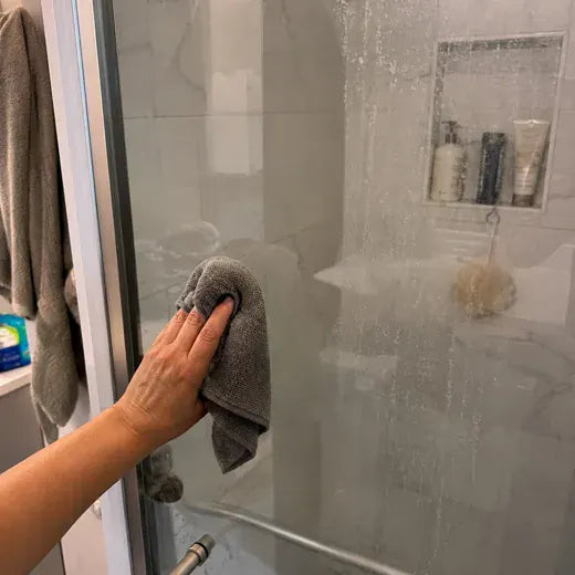 Shower glass being wiped clean after hard-water spots