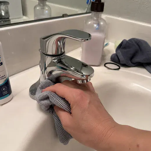 Bathroom faucet being wiped with microfiber cloth